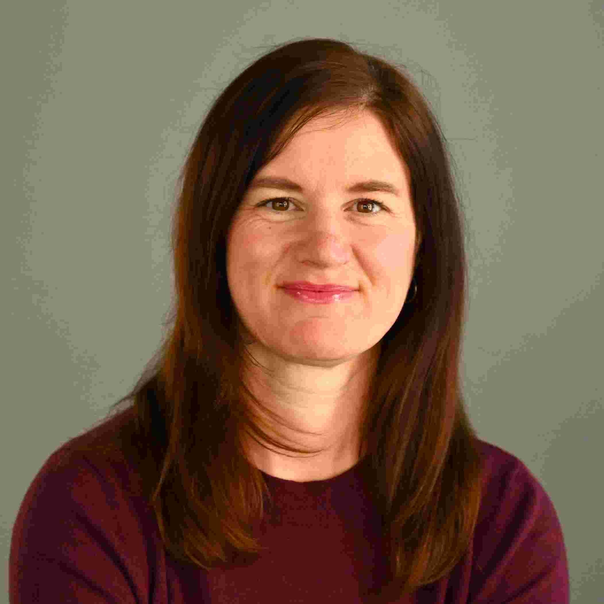 Porträt von Vicky Pohl mit langem dunkelbraunem Haar und bordeauxfarbenem Oberteil vor grauem Hintergrund.